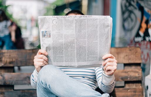 Lesende Person hält Zeitung vor dem Gesicht.